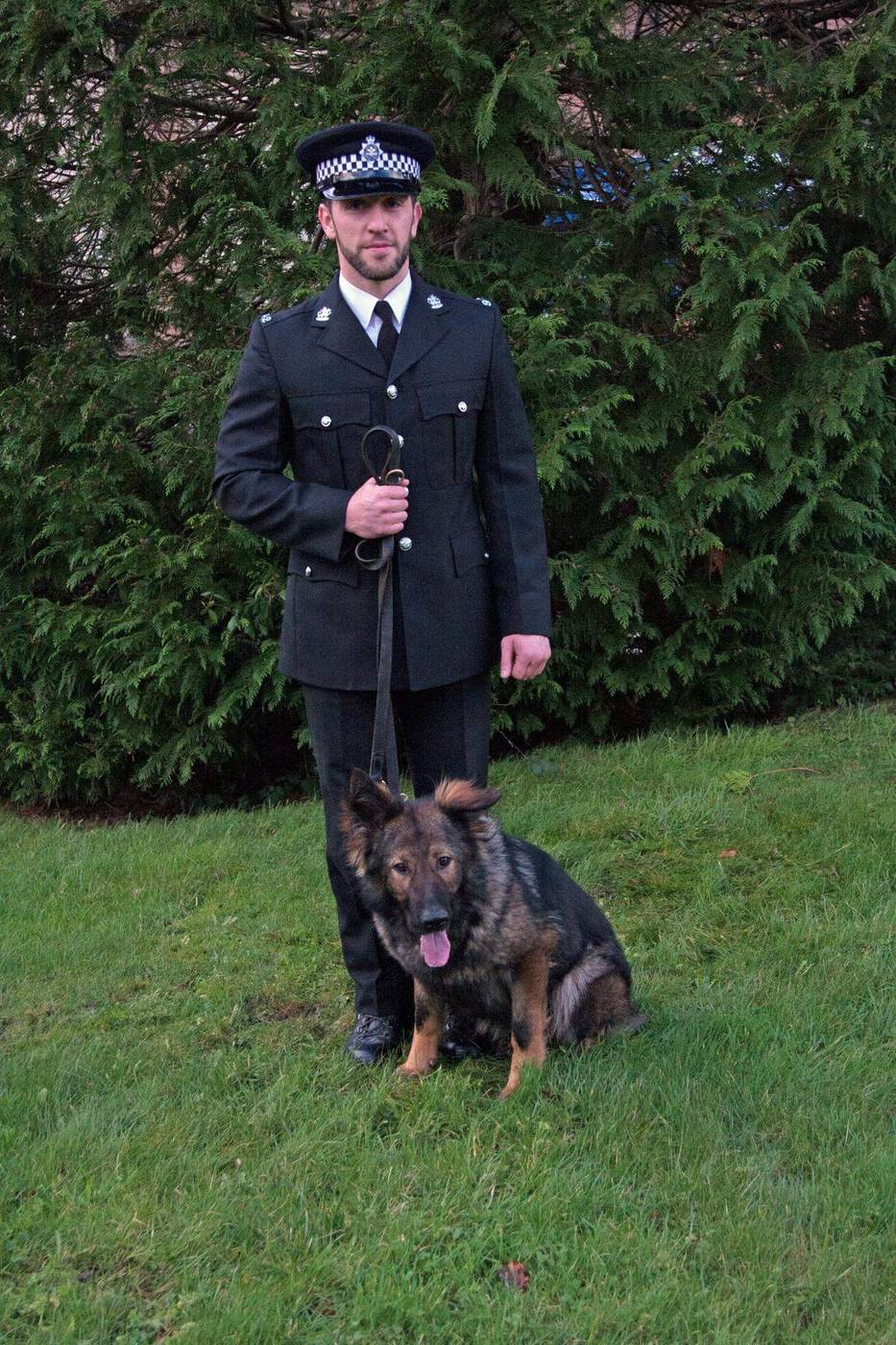 Ryan in police dress uniform with a German Shepherd police dog lying at his feet